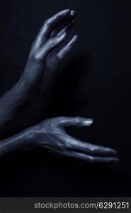 beautiful man&rsquo;s hands in silver paint on black background close up