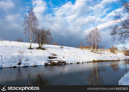 Beautiful March landscape with a small quiet river on a cloudy day.