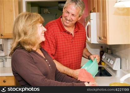 Beautiful mature couple doing dishes together and smiling.