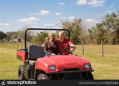 Beautiful mature couple having fun riding the farm in their all terrain vehicle. Wide view with room for text.
