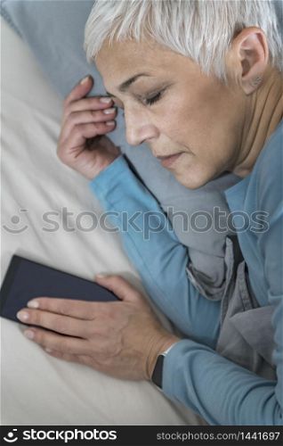 Beautiful Mature Woman Sleeping in Bed, Holding Smartphone
