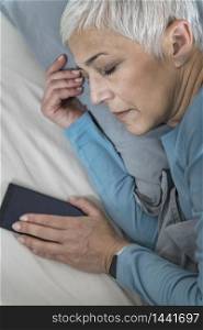 Beautiful Mature Woman Sleeping in Bed, Holding Smartphone