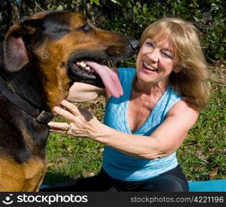 Beautiful mature woman smiles affectionately at her doberman-shepherd mixed breed dog.