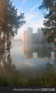 Beautiful medieval castle and moat at sunrise with mist over moat and sunlight behind castle