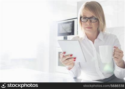 Beautiful mid adult businesswoman having coffee while using table PC at home