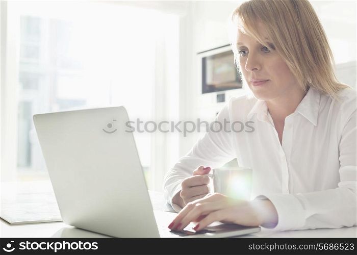 Beautiful mid adult businesswoman using laptop while having coffee at home