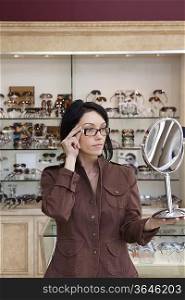 Beautiful mid adult female customer trying on glasses while looking into mirror