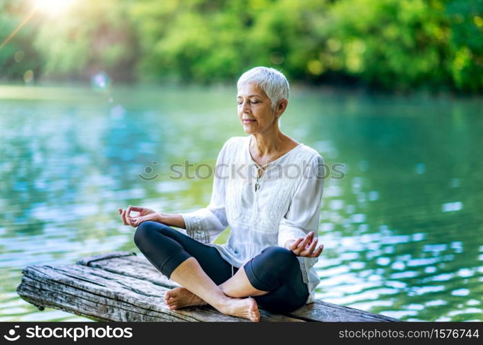 Beautiful mindful senior woman meditating by the water. Meditating by the water