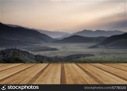 Beautiful misty mountains sunrise landscape with farm wall leading in to distance. View along countryside fields towards misty Snowdonia mountain range in distance with wooden planks floor