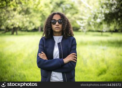 Beautiful mixed race African American girl teenager female young woman outside in spring or summer wearing sunglasses and blue jacket looking sad depressed or thoughtful