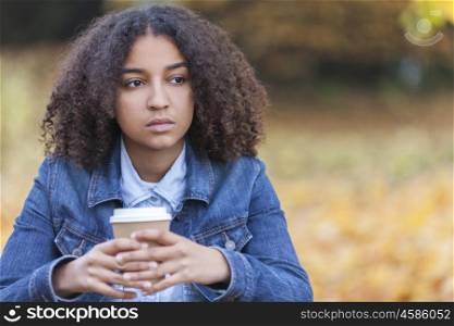Beautiful mixed race African American girl teenager female young woman outside in autumn or fall looking sad depressed or thoughtful drinking coffee