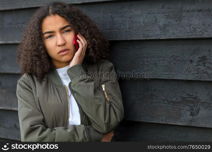 Beautiful mixed race African American girl teenager female young woman outside looking sad depressed or thoughtful talking on mobile cell phone