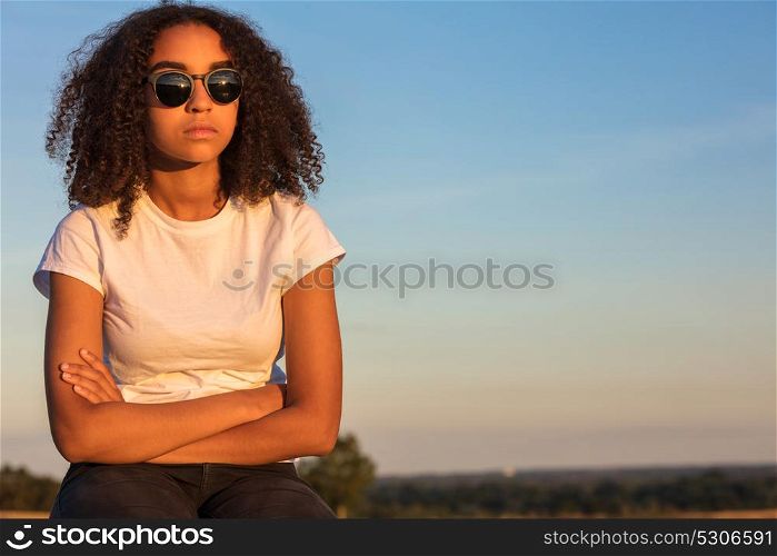 Beautiful mixed race African American girl teenager female young woman outside wearing sunglasses looking sad depressed or thoughtful at sunrise or sunset