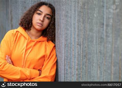 Beautiful mixed race African American girl teenager female young woman outside wearing an orange hoodie looking sad depressed or thoughtful