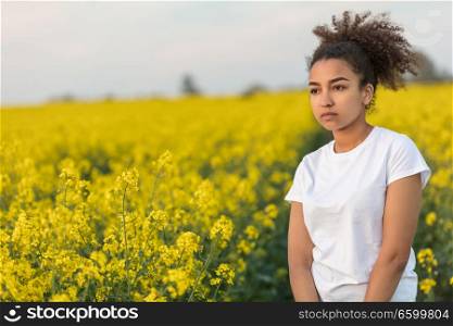 Beautiful mixed race African American girl teenager female young woman sad depressed or thoughtful at the end of a path in a field of yellow flowers