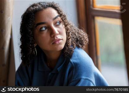 Beautiful mixed race African American girl teenager female young woman sad depressed or worried looking out of a window