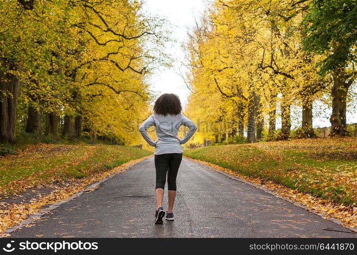 Beautiful mixed race African American young woman girl teenager preparing for fitness running jogging on road of Autumn Fall trees