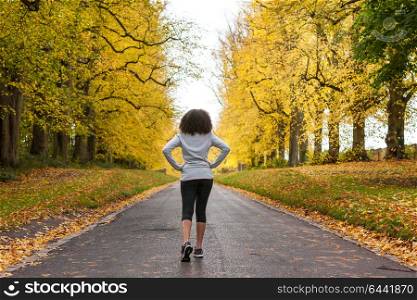 Beautiful mixed race African American young woman girl teenager preparing for fitness running jogging on road of Autumn Fall trees