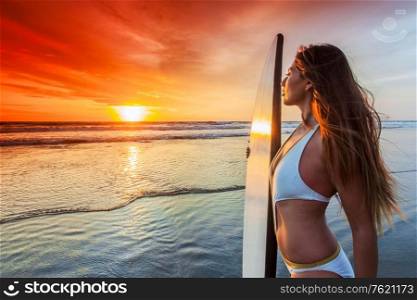 Beautiful mixed race woman on tropical beach holding surfboard at sunset. Woman on beach holding surfboard