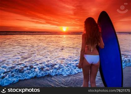 Beautiful mixed race woman on tropical beach holding surfboard at sunset. Woman on beach holding surfboard