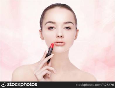 Beautiful model girl holding lipstick tube with red paint splashes on pink bokeh background
