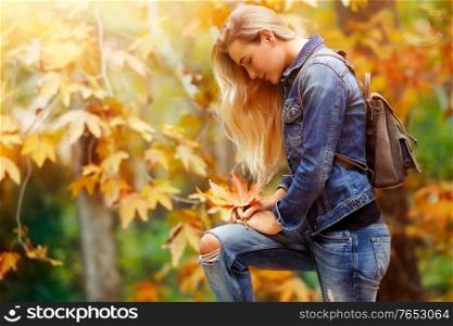 Beautiful model in autumn park, attractive female standing side view and posing over autumnal background, enjoying fall nature