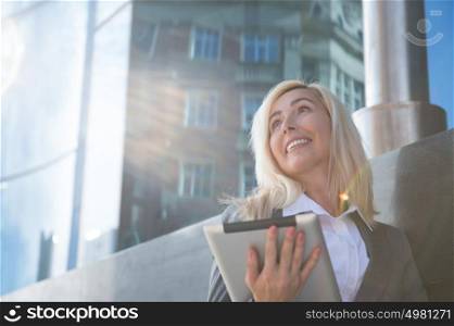 Beautiful modern businesswoman holding tablet computer with office building on background