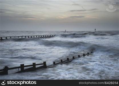 Beautiful moody stormy landscape image of waves crashing onto beach at sunrise