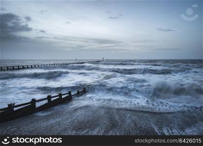 Beautiful moody stormy landscape image of waves crashing onto beach at sunrise
