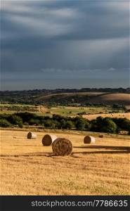 Beautiful moody Summer landscape of field of hay bales with dramatic stormy clouds overhead in English countryside