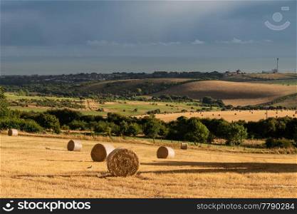 Beautiful moody Summer landscape of field of hay bales with dramatic stormy clouds overhead in English countryside
