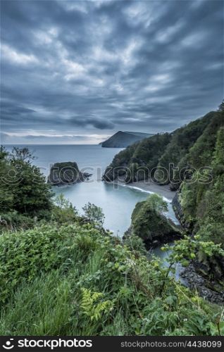Beautiful moody sunrise landsape image of small secluded cove at Combe Martin Bay