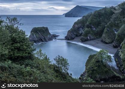 Beautiful moody sunrise landsape image of small secluded cove at Combe Martin Bay