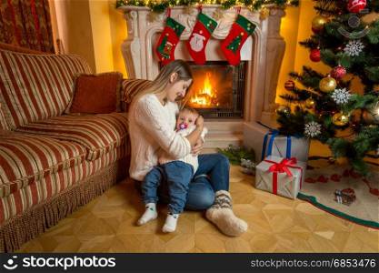 Beautiful mother and baby sitting on floor at fireplace decorated for Christmas