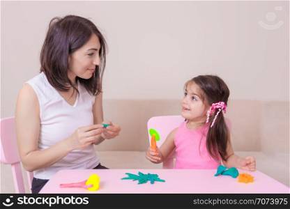 Beautiful mother and cute girl playing together with playdough while sitting on table. . Mother and Cute girl playing together with playdough
