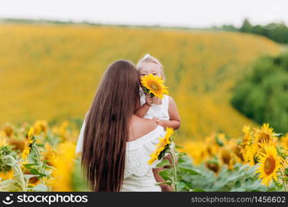 beautiful mother are hugging with the daughter in the field of sunflowers. woman with long hair and baby girl are having fun outdoors. family concept. summer holiday.. beautiful mother are hugging with the daughter in the field of sunflowers. woman with long hair and baby girl are having fun outdoors. family concept. summer holiday