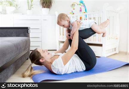 Beautiful mother doing yoga exercise with her baby on floor at living room