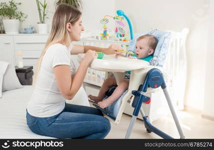 Beautiful mother feeding her baby in highchair at living room