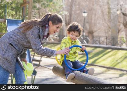 Beautiful mother teaches her adorable little son how to play on a wooden seesaw. Family and fun concept.. Mother and son having fun on a seesaw