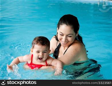 Beautiful mother teaching cute baby girl how to swim in a swimming pool. Child having fun in water with mom.