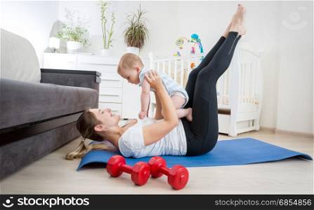 Beautiful mother with her baby doing physical exercises on fitness mat