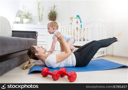 Beautiful mother with her baby doing physical exercises on fitness mat at living room