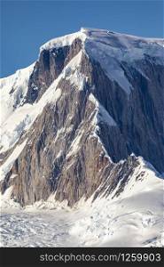 Beautiful mountain peak made of rock covered with vertical ridges and glaciers