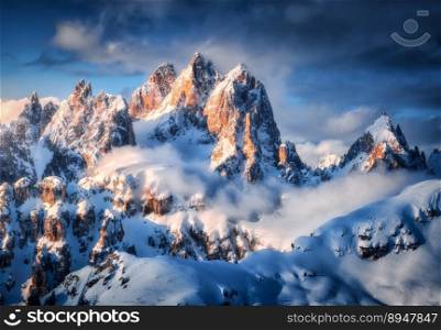 Beautiful mountain peaks in snow in winter at sunrise. Colorful landscape with high snowy rocks  in fog, blue sky with clouds in cold evening. Tre Cime in Dolomites, Italy. Alpine mountains. Nature