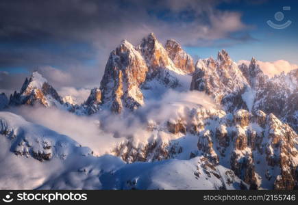 Beautiful mountain peaks in snow in winter at sunset. Colorful landscape with high snowy rocks in fog, blue sky with clouds in cold evening. Tre Cime in Dolomites, Italy. Alpine mountains. Nature