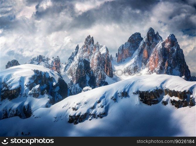 Beautiful mountain peaks in snow in winter. Dramatic landscape with high snowy rocks, overcast sky with clouds in cold evening. Tre Cime in Dolomites, Italy. Alpine mountains. Nature. Dark scenery