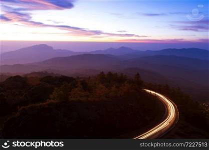 Beautiful mountain road at dawn, curvy mountain road with light trails against sunrise sky in the background. Long exposure.
