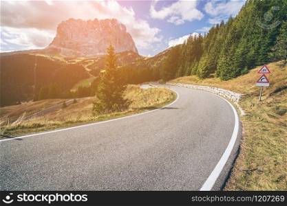 Beautiful mountain road with trees, forest and mountains in the backgrounds. Taken at state highway road in Passo Gardena, Langkofel mountain group of Dolomites mountain in Italy.
