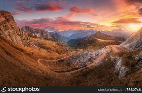 Beautiful mountains and pink sky at sunset in autumn. Nature in Dolomites, Italy. Colorful panoramic landscape with rocks, orange grass in hills, trail, dirt road, stones, sky with clouds in fall