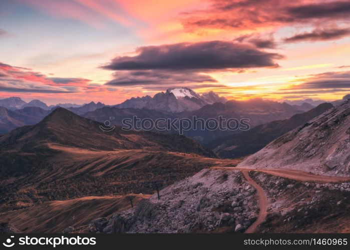 Beautiful mountains at sunset in autumn in Dolomites, Italy. Landscape with rocks, sunbeams, forest, hills with orange grass and trees, colorful red sky. Scenery with mountain valley in fog in fall